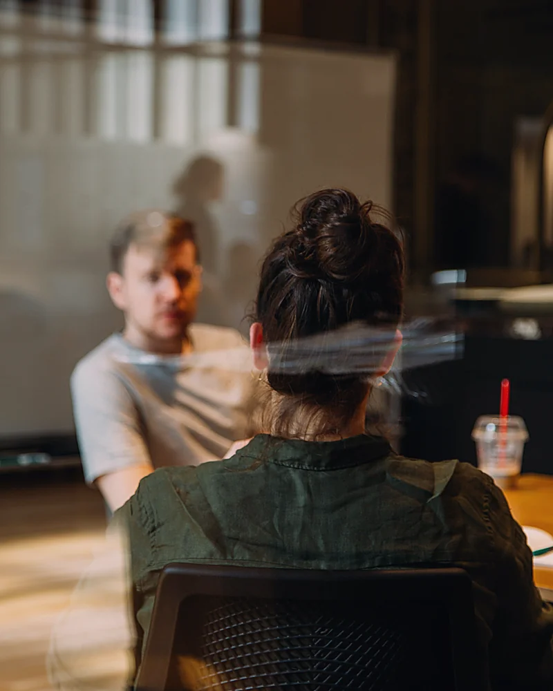 A website planning consultation between a consultant and a business owner, seen through the meeting room glass